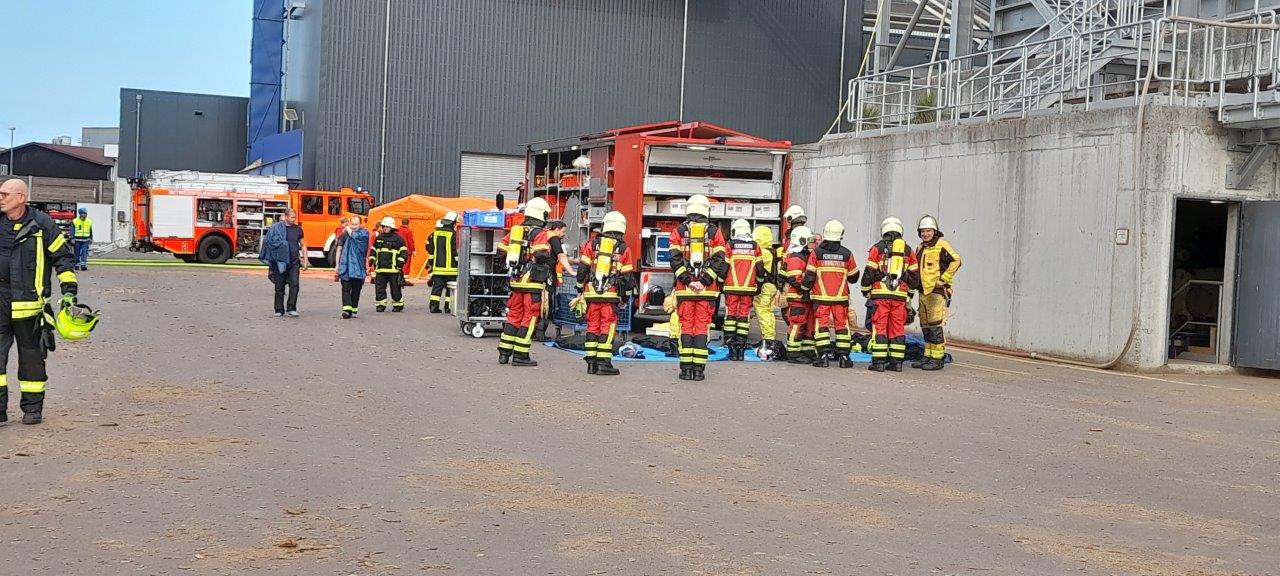 Eine Gruppe von Feuerwehrleuten steht in Arbeitskleidung auf einem Gelände