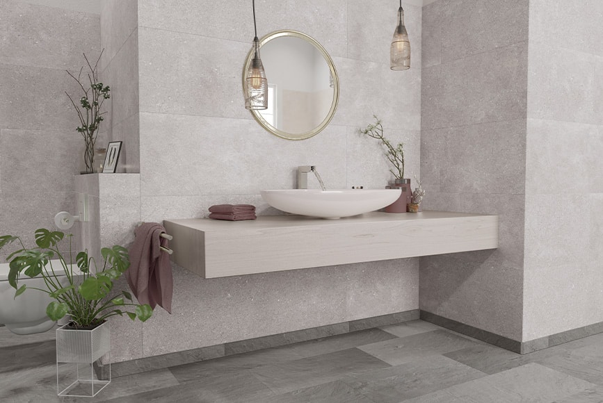 Badezimmer mit grauen Fliesen und rundem Spiegel über Waschbecken