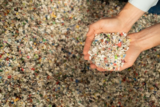 Zwei Hände halten eine Portion bunt gemischtes Ceramin®-Rezyklat, im Hintergrund eine große Menge des Materials